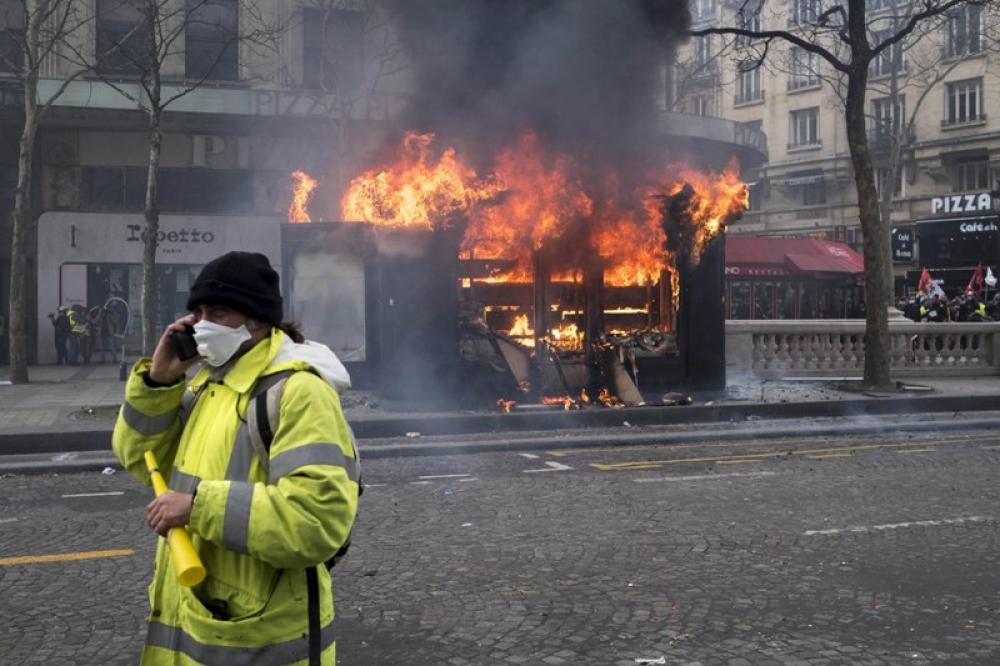 A Yellow Vest protester walks by a burning shop in Paris